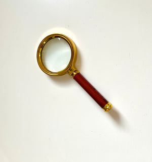 Magnifying glass with a gold-colored frame and a polished wooden handle on a plain white background