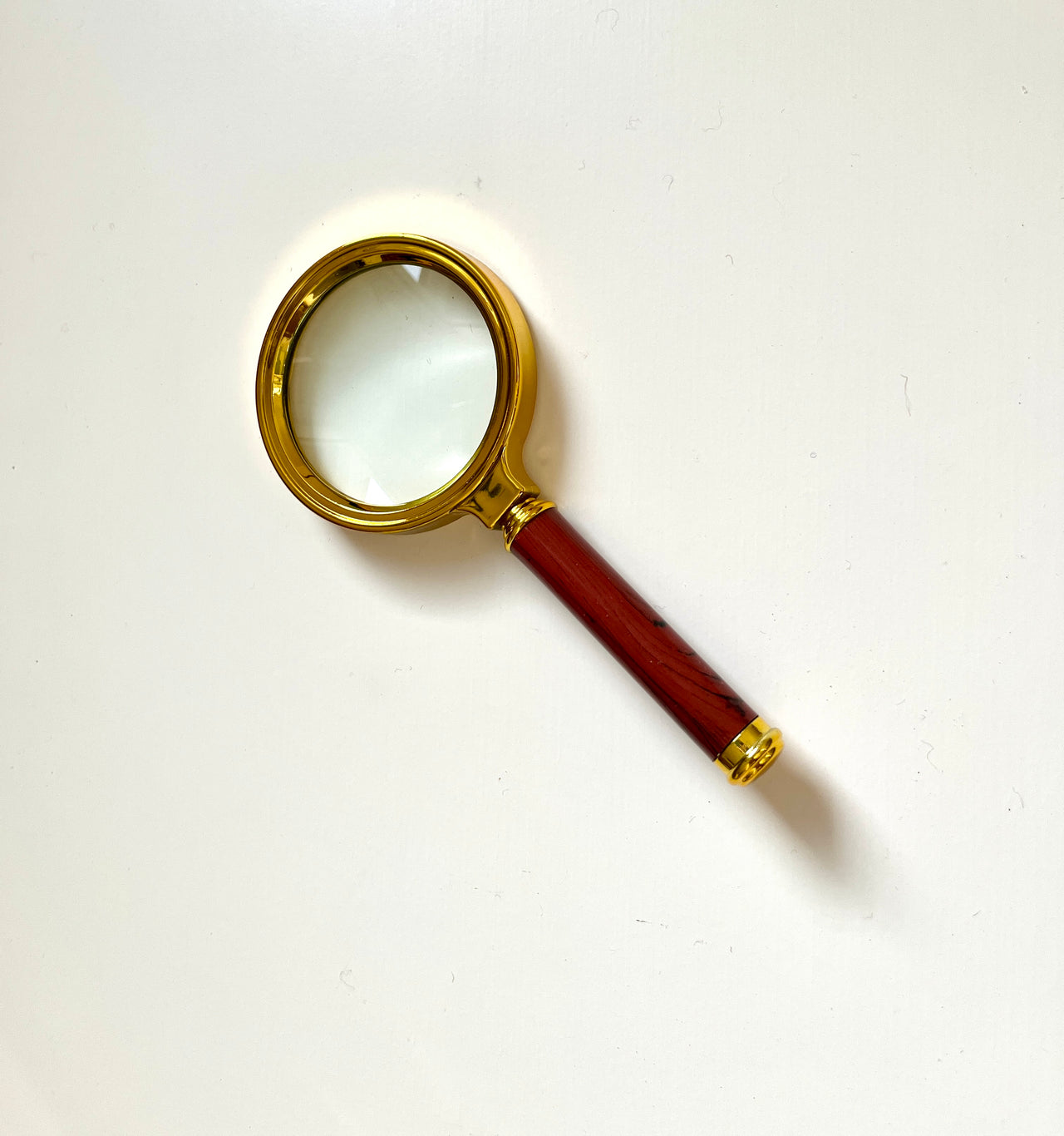 Magnifying glass with a gold-colored frame and a polished wooden handle on a plain white background