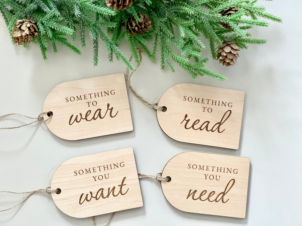Set of four maple plywood Christmas gift tags engraved with "Something you want," "need," "read," and "wear" with pine decoration