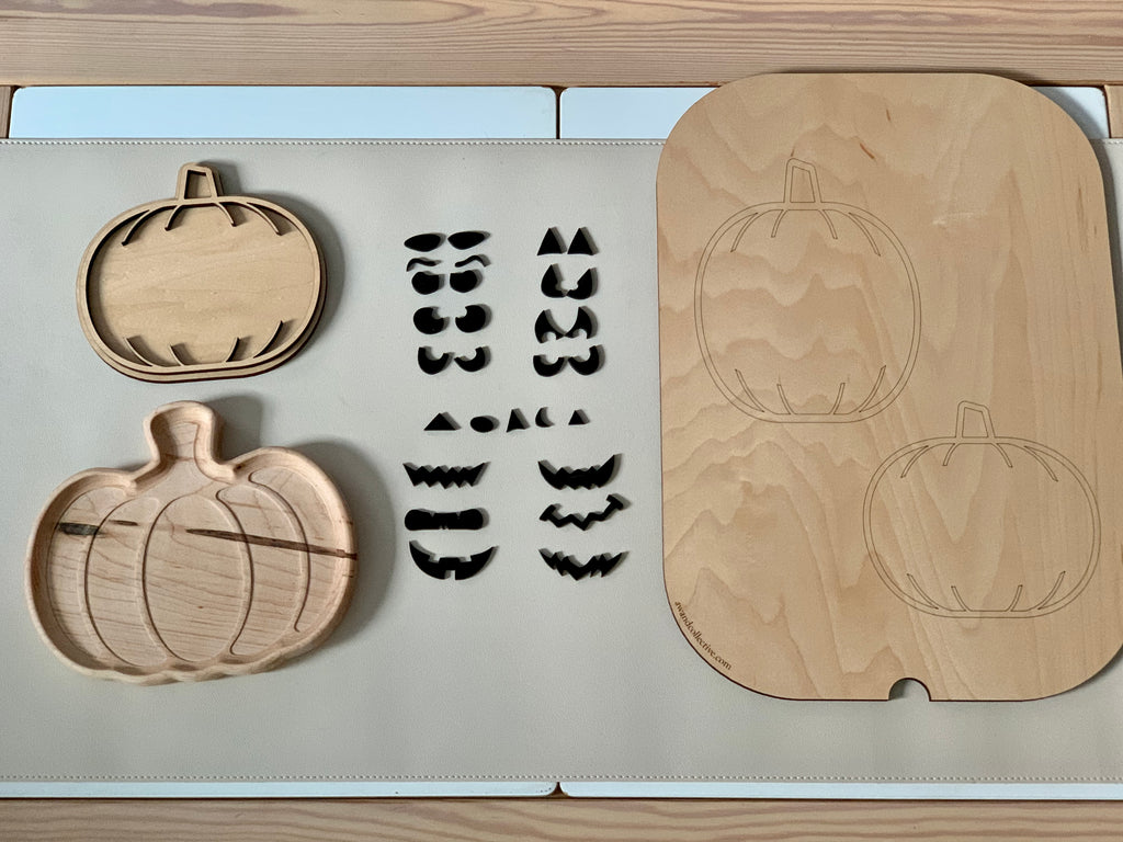 Wooden pumpkin-shaped inserts and various black eyebrow and mouth pieces arranged on a beige surface next to pumpkin outlines