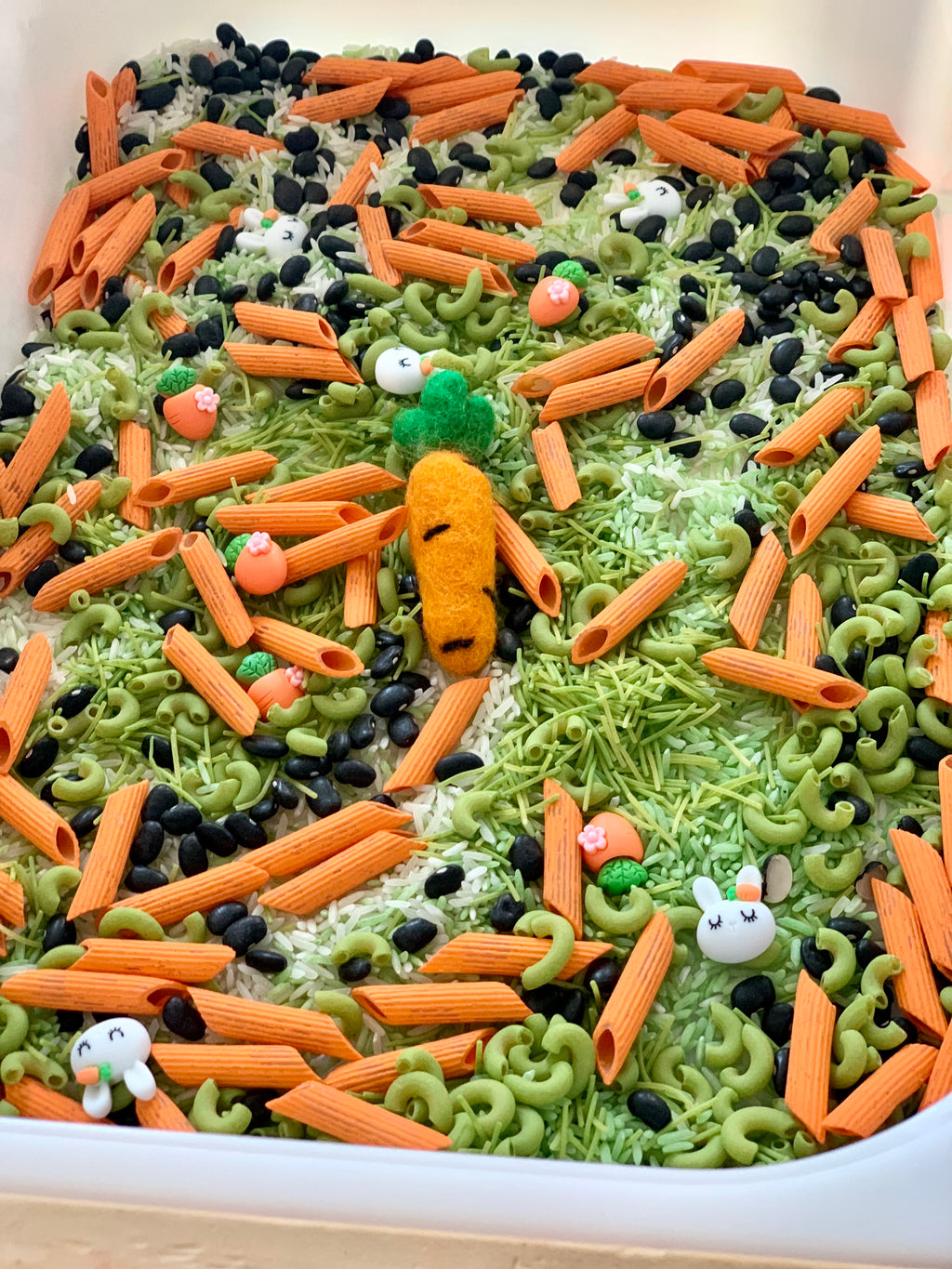 White container filled with green and orange pasta, black beans, rice, and small carrot and bunny shapes scattered on top