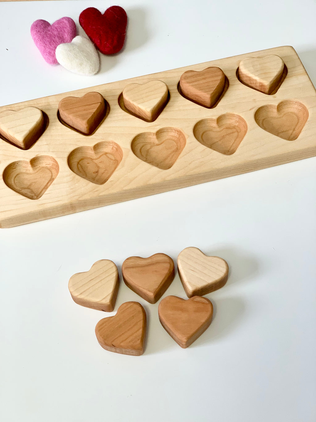 Light and dark wooden heart-shaped blocks with matching recesses on a natural wood tray and three felt hearts nearby