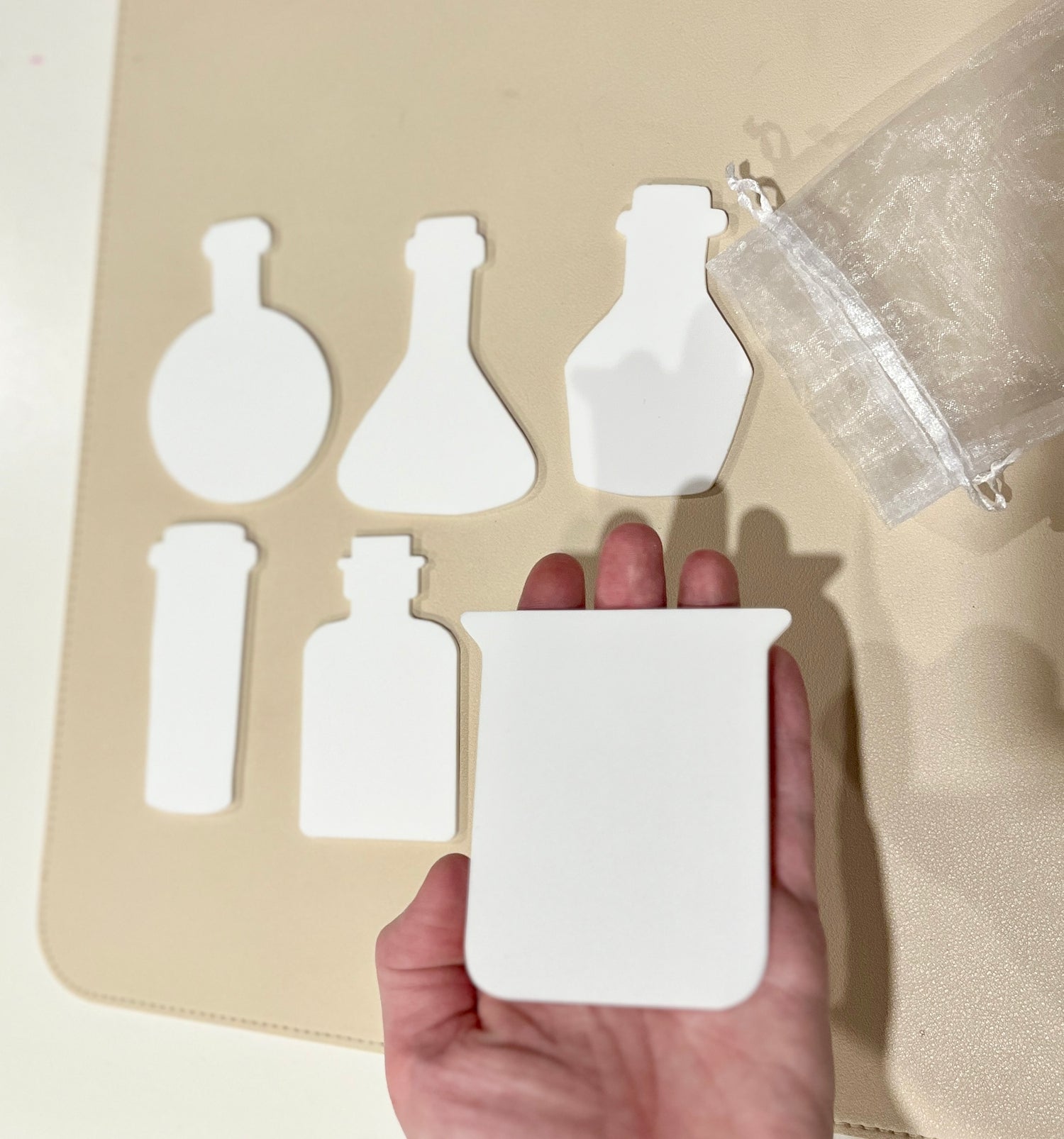 Set of six white dry erasable beaker and potion bottle shapes with a sheer drawstring pouch on pale surface