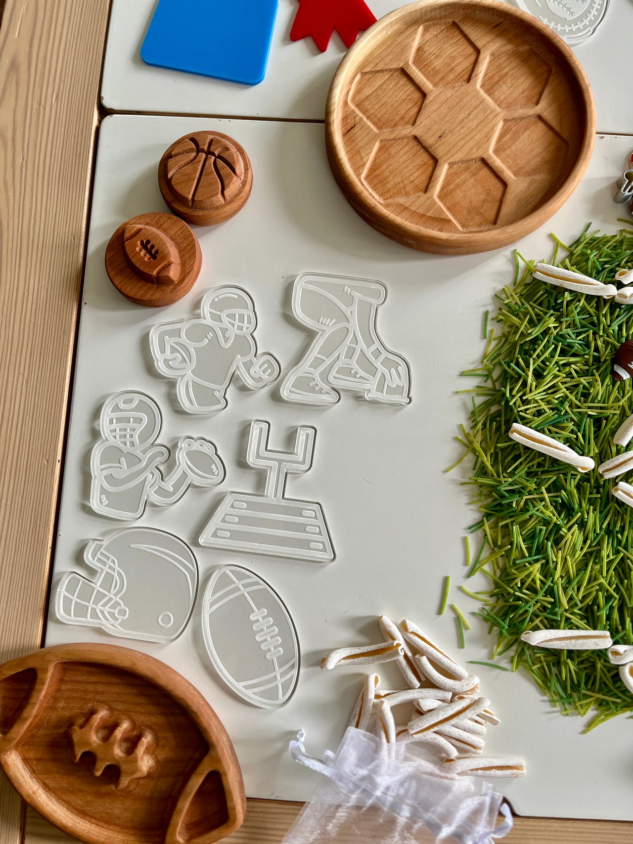 Clear plastic cookie cutters shaped like football players, helmet, goalpost, and football with wooden trays and green craft grass