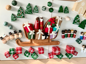 Hand-painted wooden Christmas peg dolls with Santa, Mrs Claus, snowmen, reindeer, elves, gifts, trees, and decorations on white surface