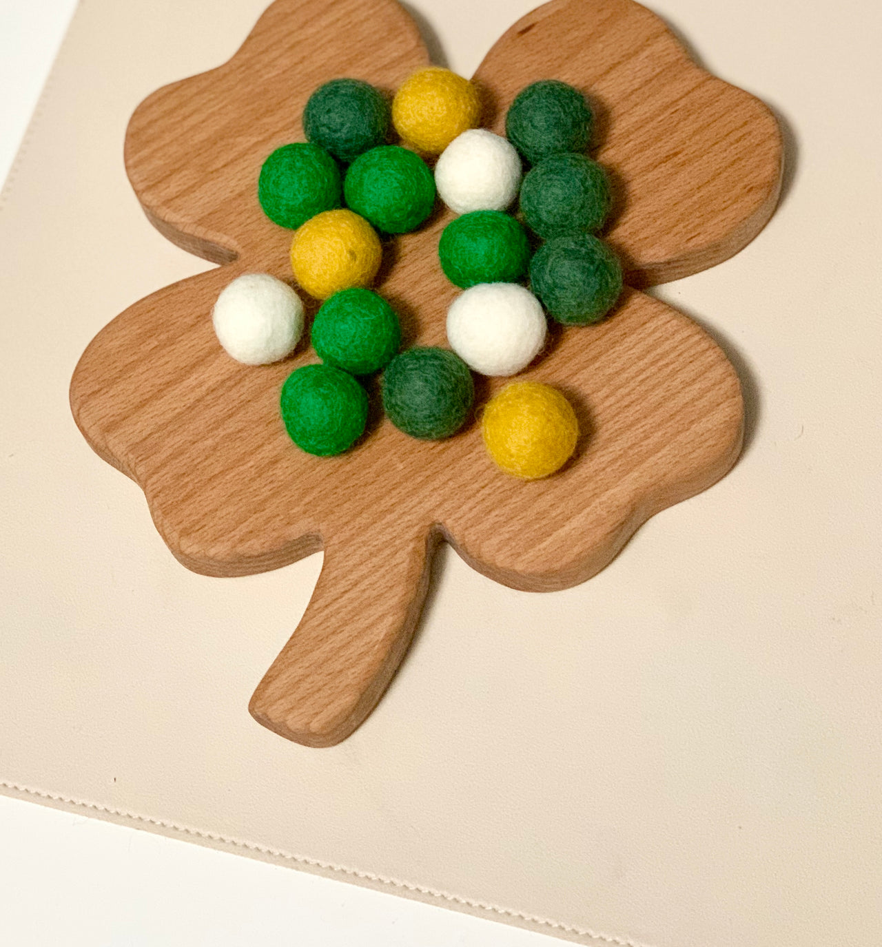Wooden four-leaf clover-shaped board holding green, white, and yellow felt balls on a beige surface