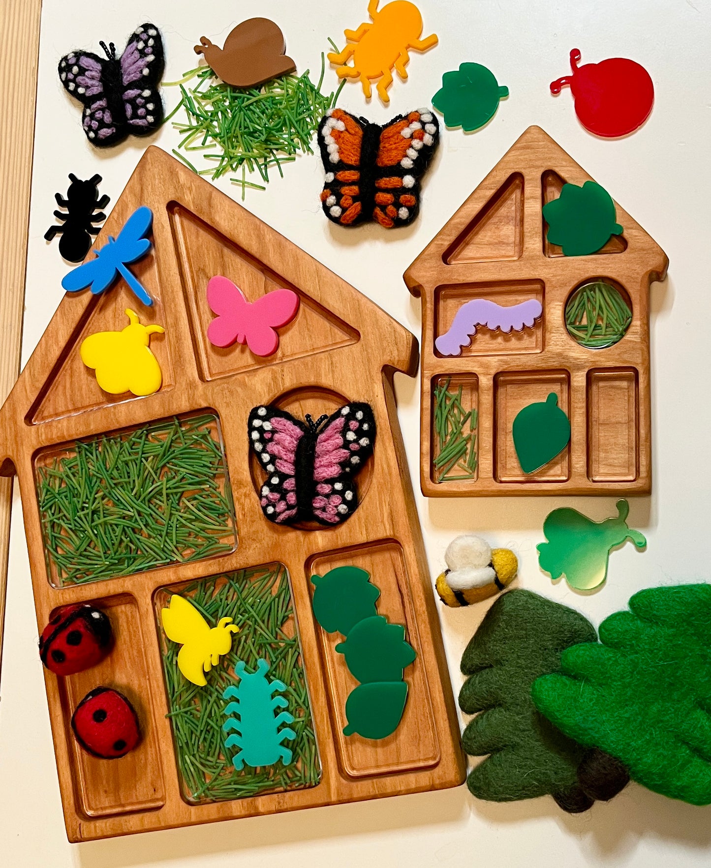 Wooden house shaped educational tray with compartments, with nature-themed felt and acrylic pieces including leaves, butterflies, and a bee on a light background.