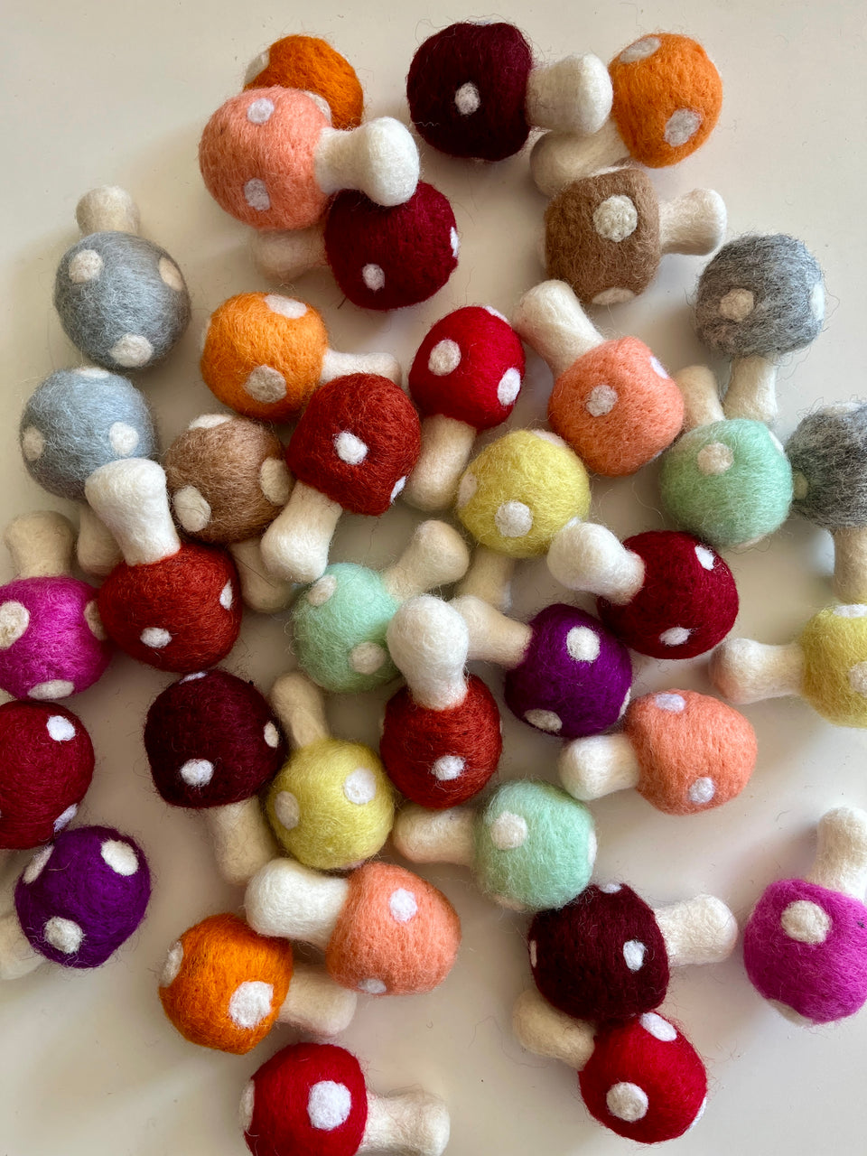 Various small felt mushrooms in multiple colors with white spots scattered on a light surface