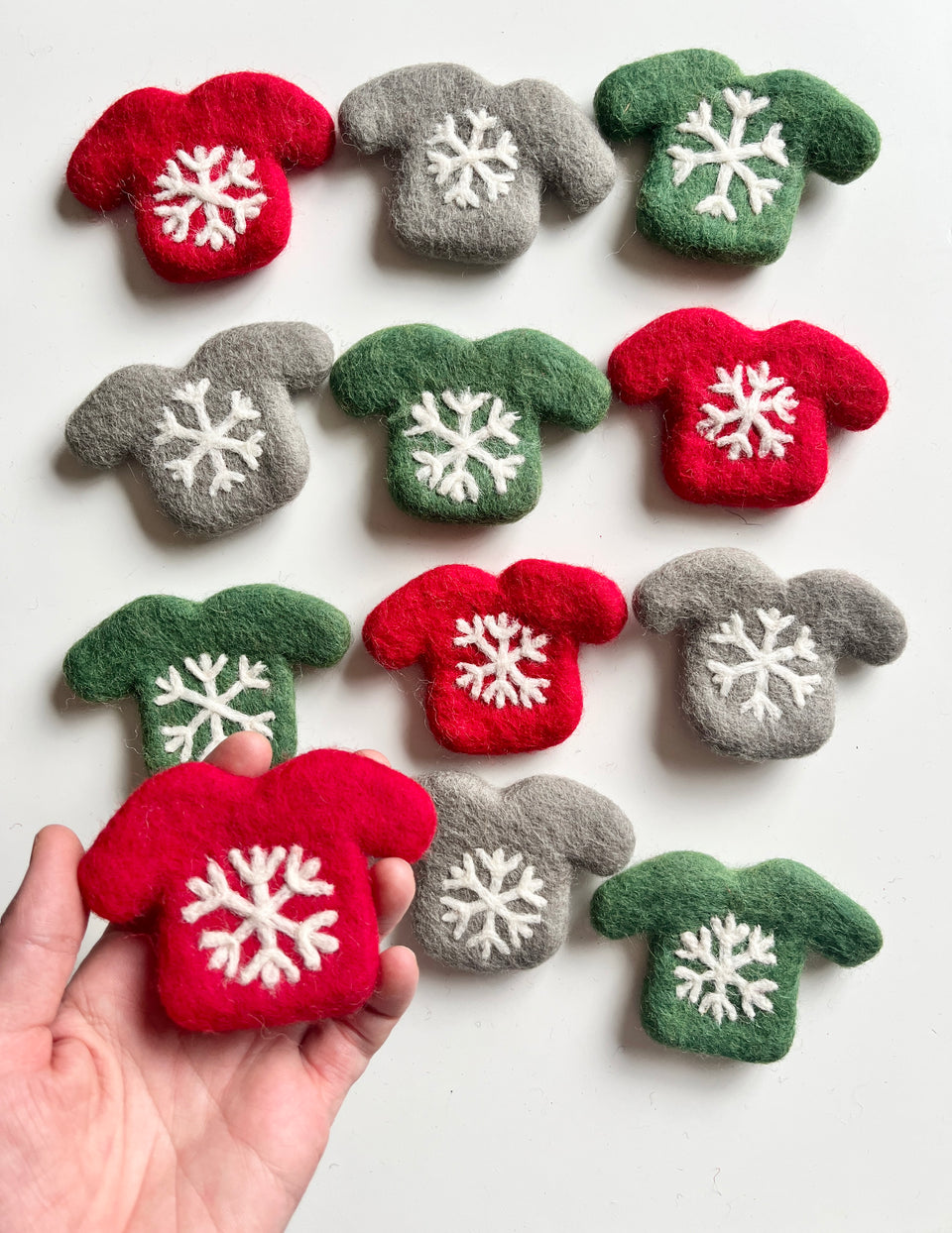 Felt miniature Christmas sweaters in red, green, and gray with white snowflake designs on white background
