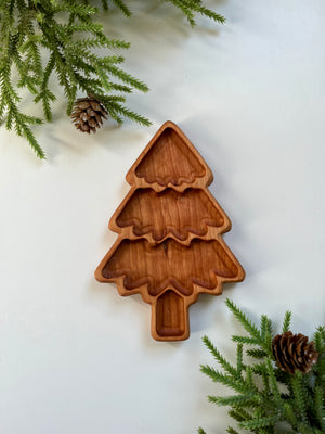 Carved wooden tray shaped like a layered Christmas tree with pine branches and pine cones on white surface