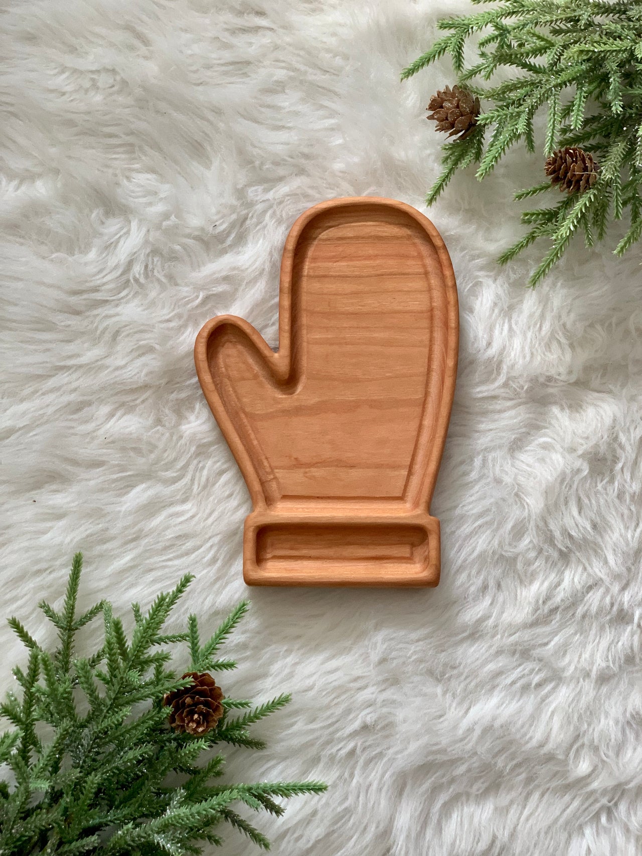 Wooden mitten-shaped sensory tray on fluffy white surface with pinecones and evergreen sprigs nearby