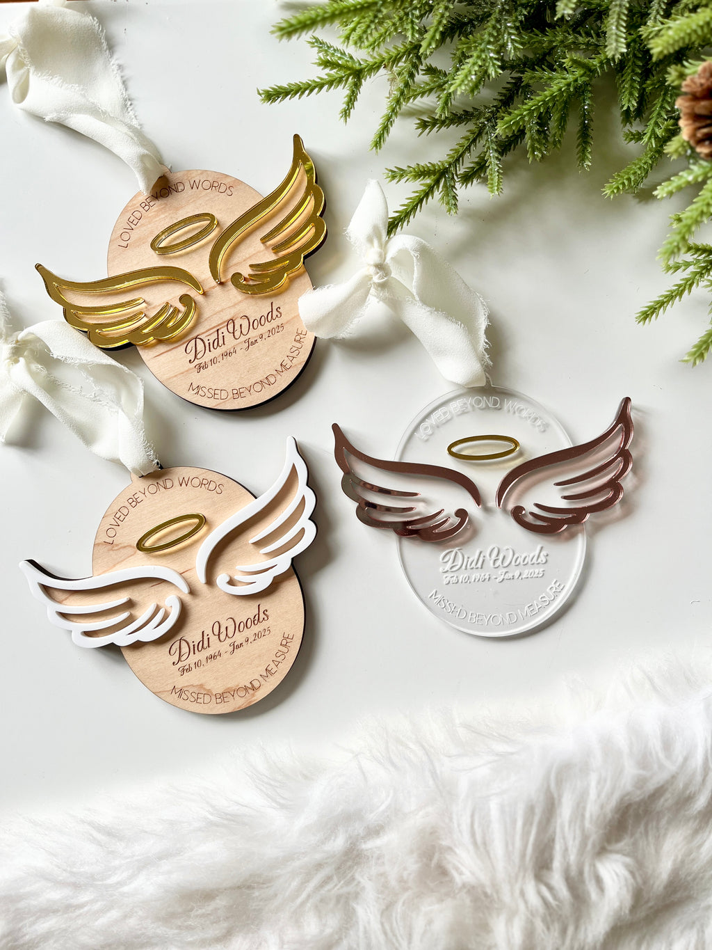 Three acrylic angel wing ornaments in gold, white, and bronze tones with halos on engraved wooden and clear bases