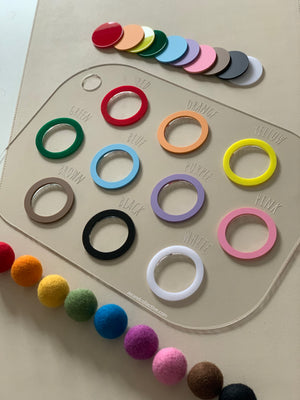 Clear acrylic colour sorting lid with labeled colored rings and matching felt balls on beige surface