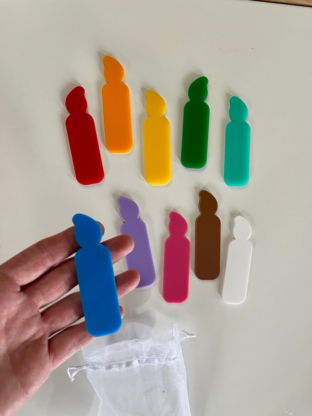 Set of colorful flat candle-shaped tokens in red, orange, yellow, green, teal, blue, purple, pink, brown, and white with a white drawstring pouch
