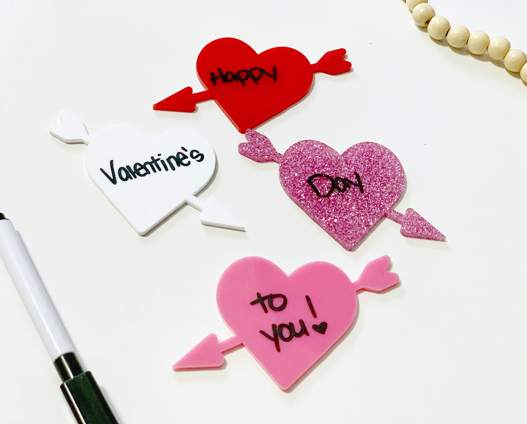 Four heart-shaped dry erase boards in red, pink, glitter pink, and white with arrows and handwritten Valentine’s message