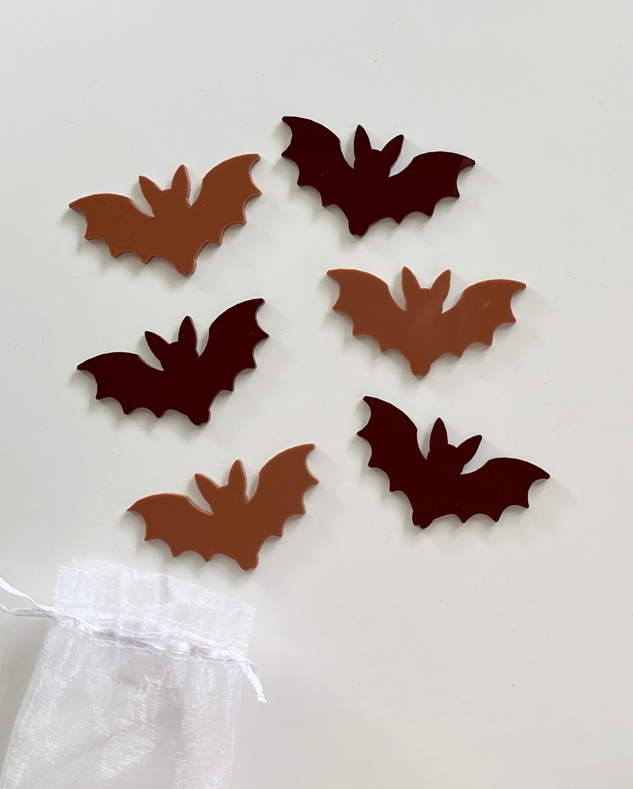 Six flat bat-shaped cutouts in alternating dark brown and light tan colors displayed near a small white organza bag
