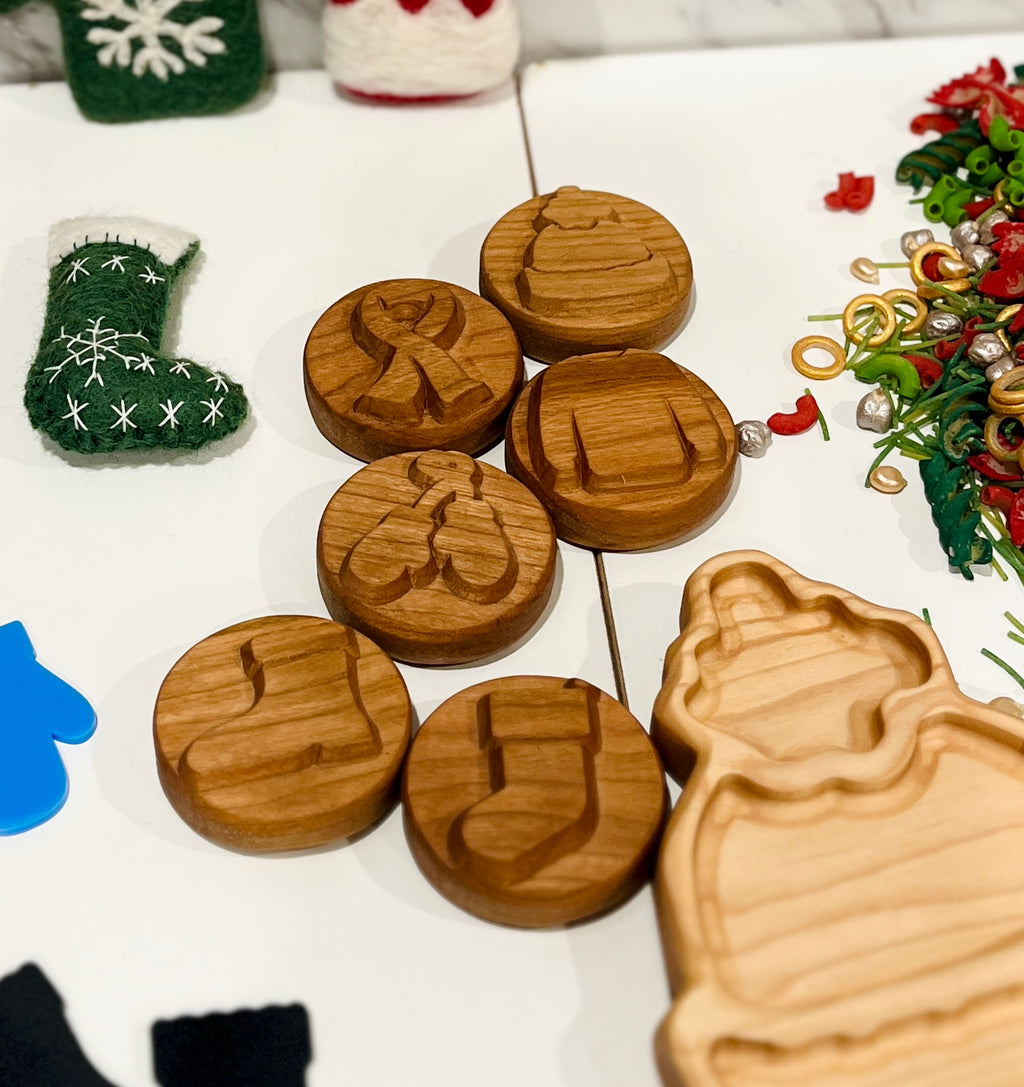 Wooden circular stamps with winter and holiday motifs surrounded by felt decorations and colorful craft pieces on white surface
