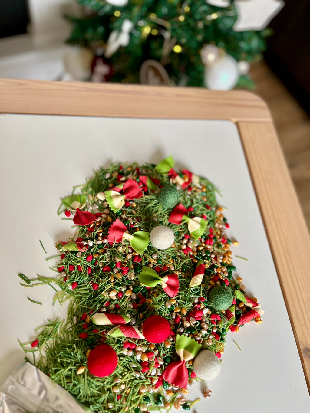 Assorted colorful birdseed and decorative red, green, and white bows and pom-poms scattered on a wooden framed board