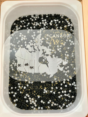Sensory bin filled with black and white beads featuring a clear map of Canada with labeled provinces inside the container