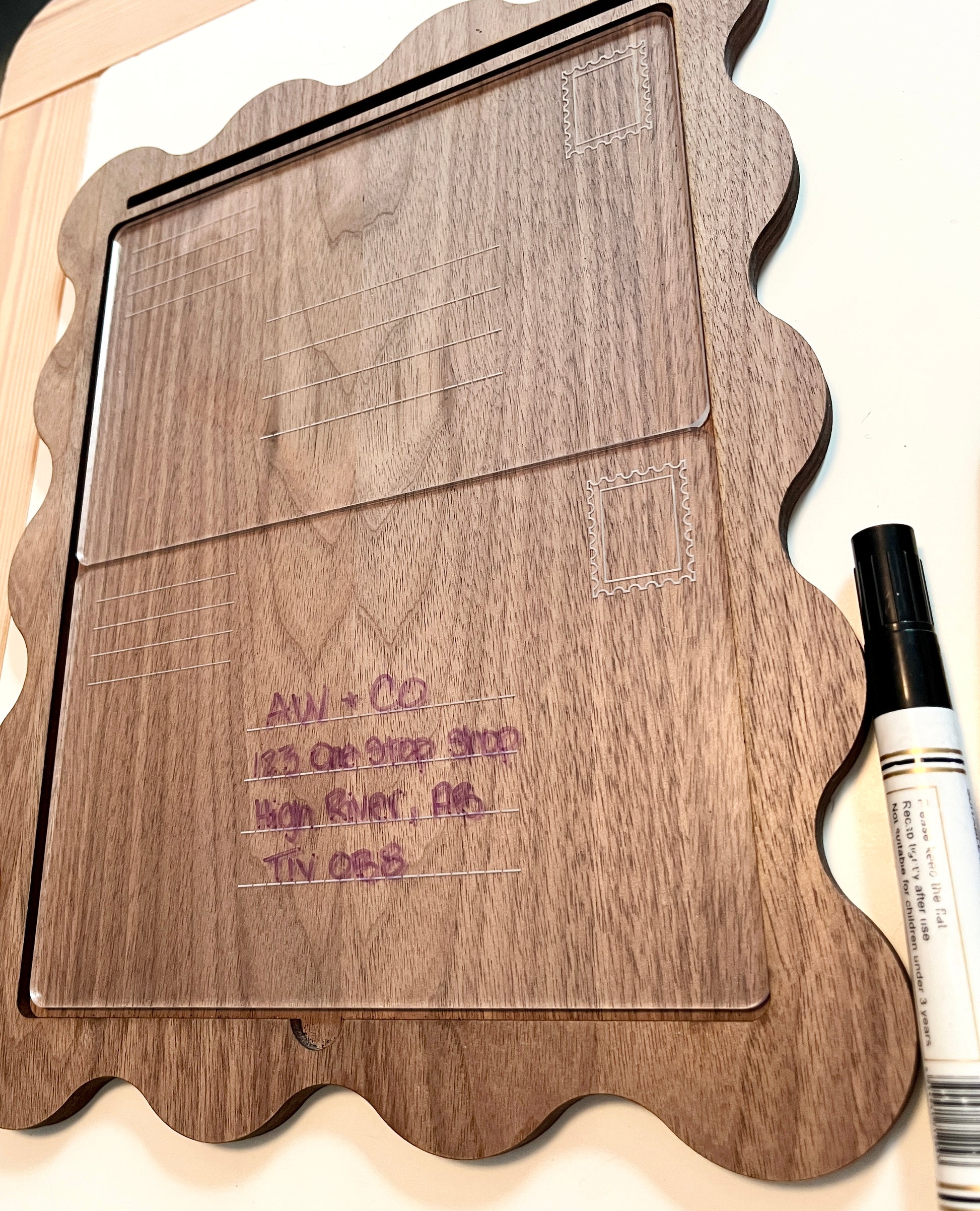 Dry erase envelope inside of a wooden tray for address practice with writing and markers on a flat surface