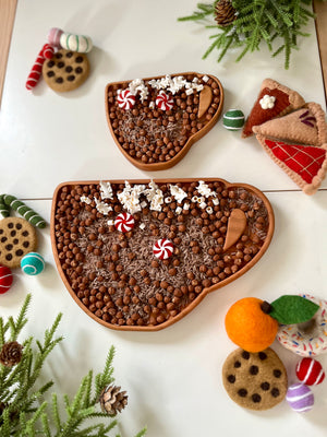 Two wooden trays shaped like coffee cups filled with chocolate beads, popcorn, peppermint candies, and small wooden scoops
