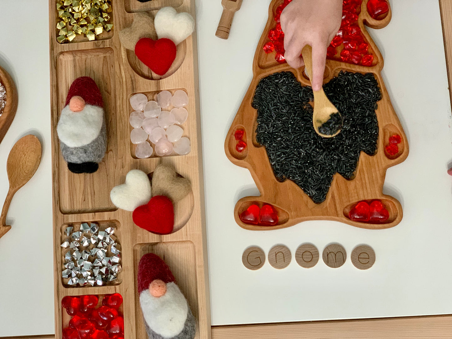 Wooden sensory tray shaped like a gnome with colored rice and small heart decorations on white surface