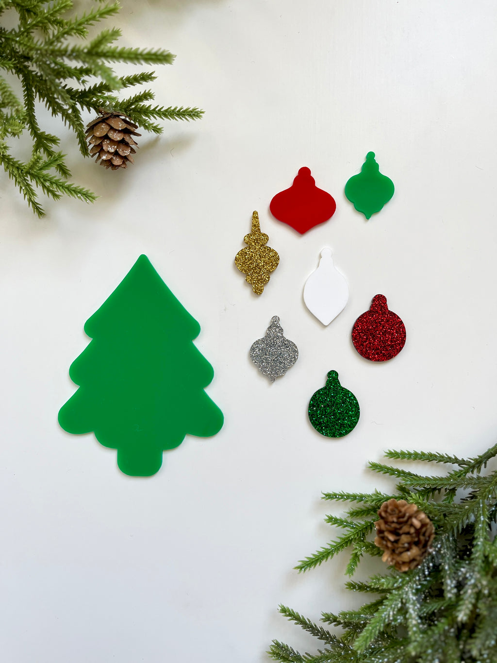 Green Christmas tree cutout surrounded by assorted red, green, white, gold, and silver glittery ornament shapes on white background