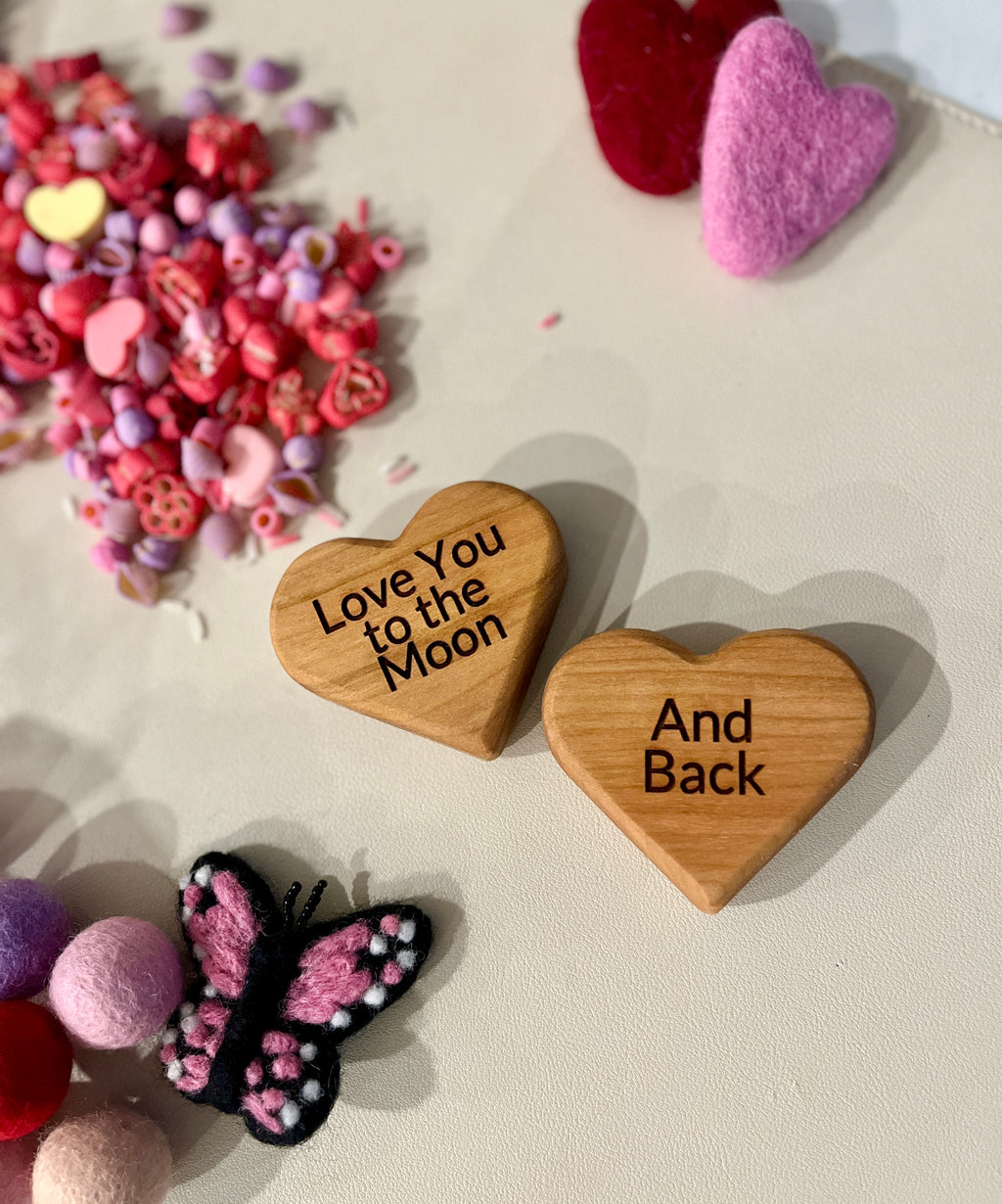 Two small wooden hearts engraved with "Love You to the Moon" and "And Back" surrounded by colorful felt hearts and beads