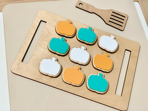 Wooden cookie sheet with orange, teal, and white pumpkin-shaped cookies and a wooden spatula on beige surface