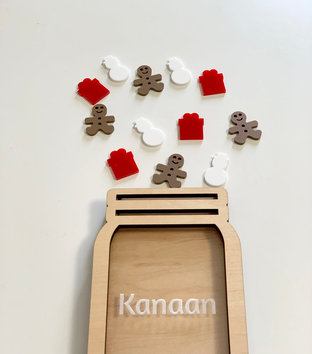 Wooden personalized reward jar with name and scattered holiday-themed tokens including gingerbread, gifts, and snowmen