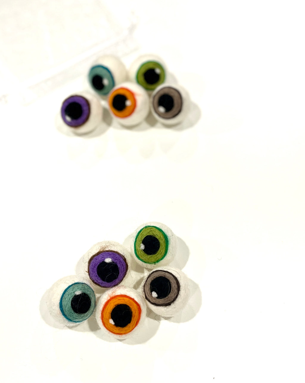 Two small clusters of round felt eyeball shapes in various colors on a white surface with soft shadows