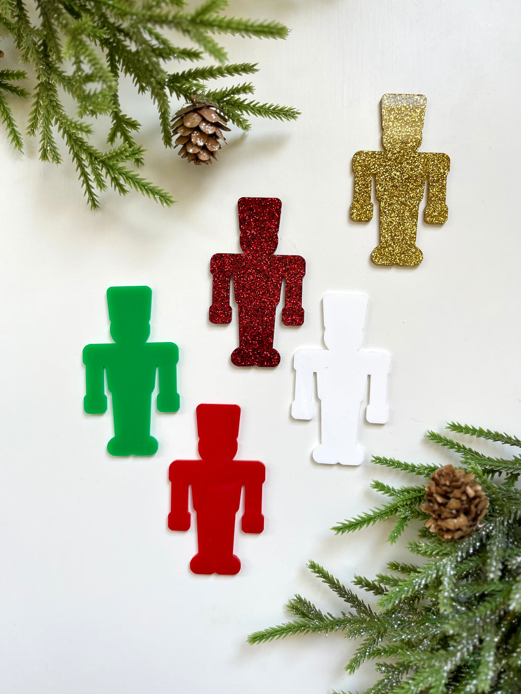Five robot-shaped cutouts in red, green, white, and glittery gold and red surrounded by pine branches and pinecones on white background