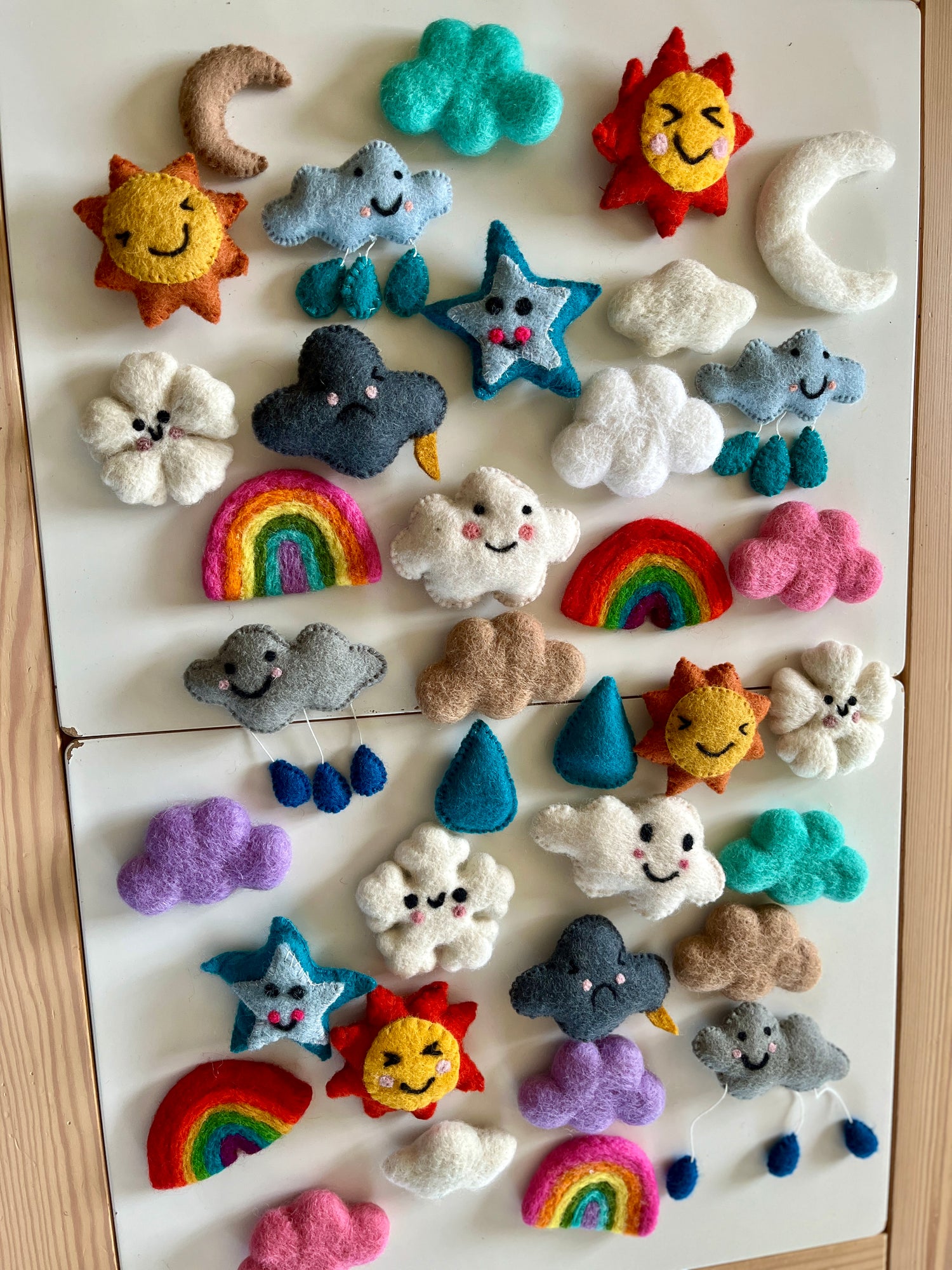 Assorted handmade felt weather shapes including clouds, suns, moons, stars, raindrops, and rainbows on white background