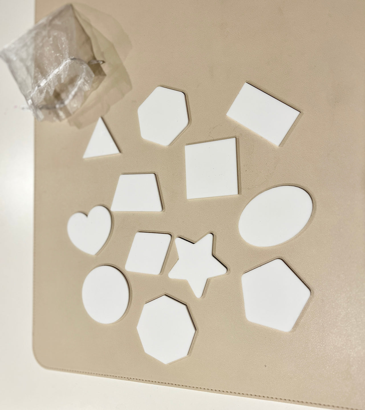 Assorted white wooden shapes including heart, star, hexagons, oval, circle, rectangle, square, and triangle on a beige surface