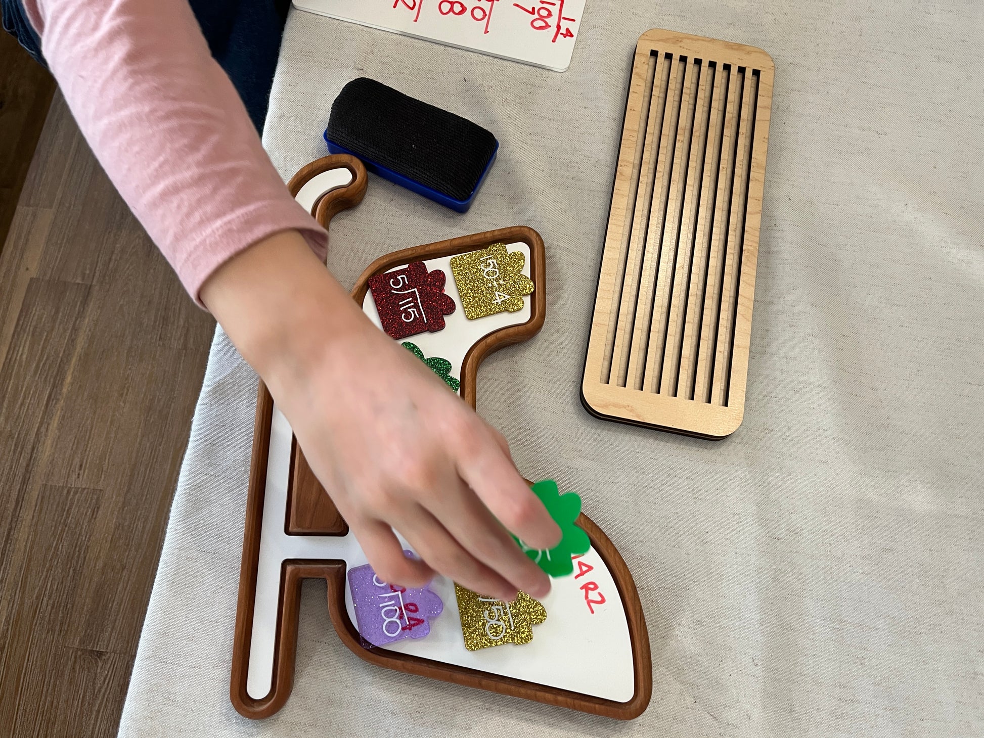 Child's hand interacting with wooden sled-shaped sensory tray featuring felt shapes and a wooden lid on light fabric surface