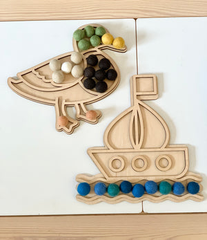 Wooden duck-shaped and boat-shaped play trays with colorful felt balls on white and wood surface