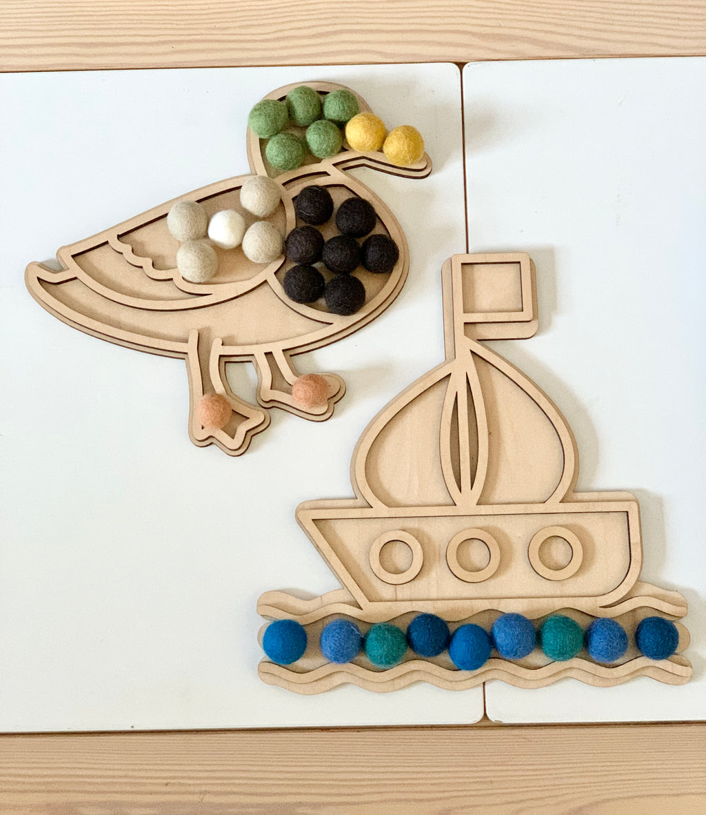 Wooden duck-shaped and boat-shaped play trays with colorful felt balls on white and wood surface