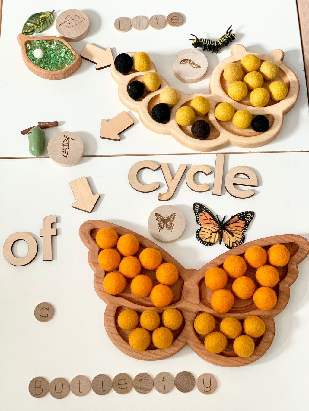 Wooden caterpillar-shaped sensory tray with yellow and black felt balls, wooden life cycle pieces, and butterfly tray with orange felt balls