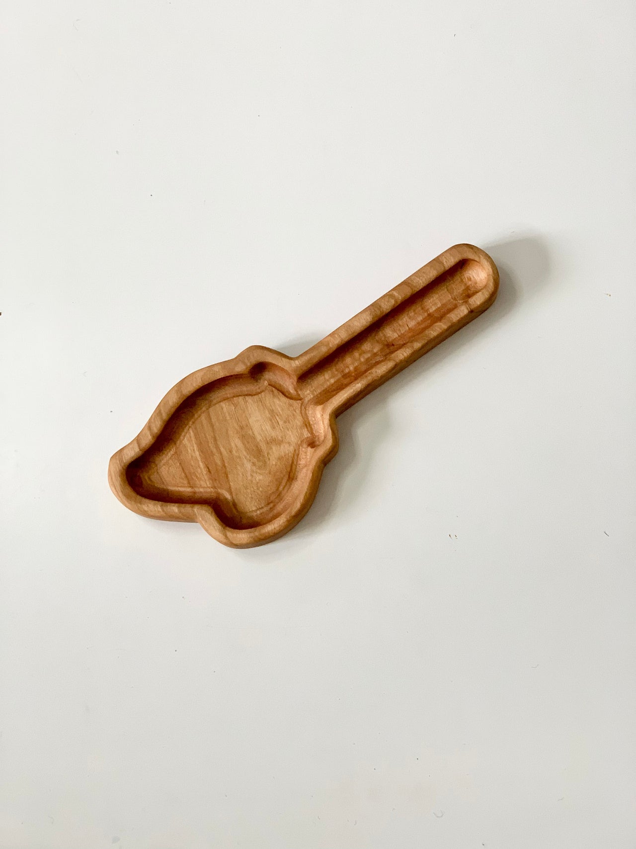 Light wooden tray carved in the shape of a scoop with smooth rounded edges on a white background