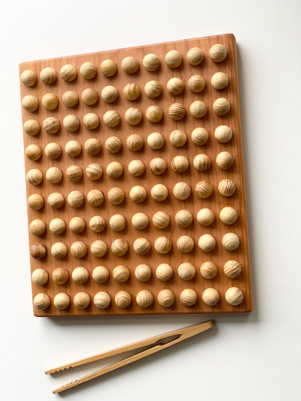 Wooden sensory board with 100 round wood balls and a pair of wooden tongs on white background