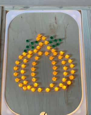 Wooden Flisat insert with light-up pegs arranged in a glowing pumpkin shape with green leaf pegs on wood surface