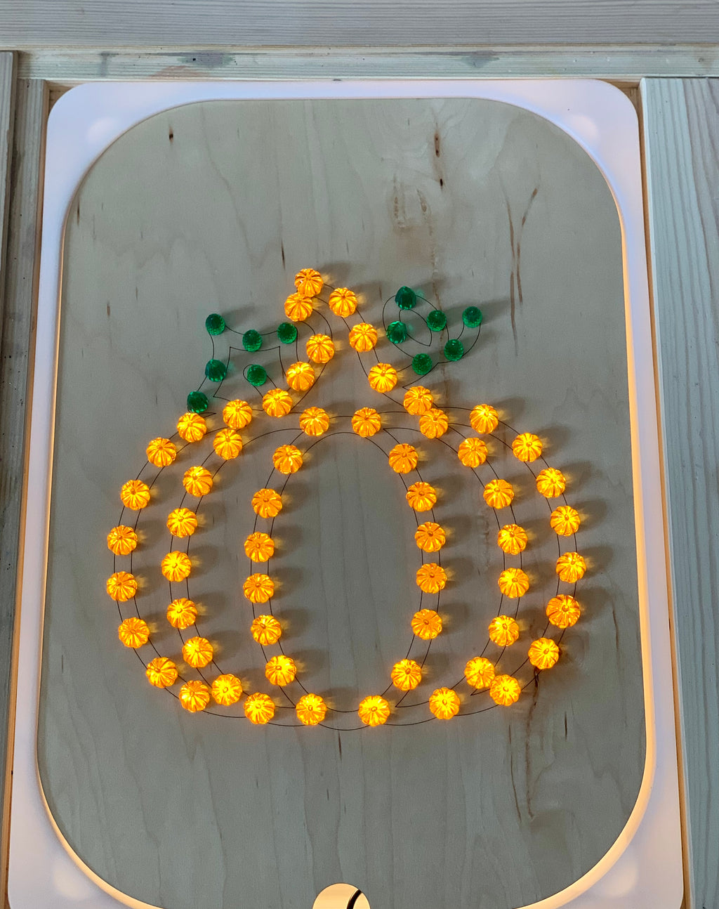 Wooden Flisat insert with light-up pegs arranged in a glowing pumpkin shape with green leaf pegs on wood surface
