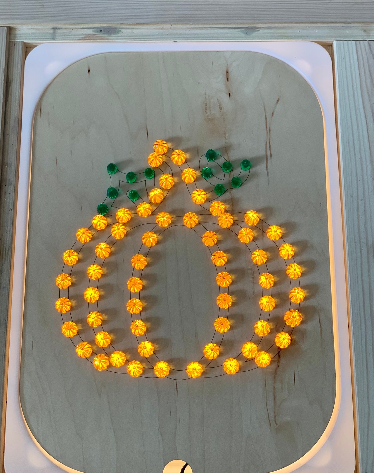 Wooden Flisat insert with light-up pegs arranged in a glowing pumpkin shape with green leaf pegs on wood surface
