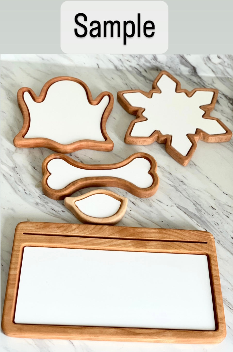 Set of wooden sensory trays in ghost, snowflake, bone, chicken drumstick, and rectangular shapes on marble surface