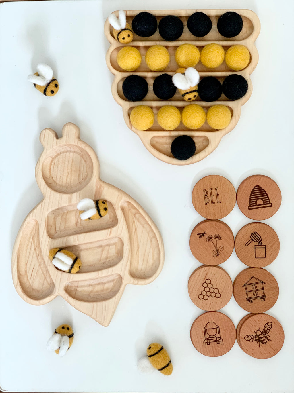 Wooden bee-shaped tray with felt bee tokens and yellow and black felt balls arranged in honeycomb-shaped tray with wooden engraved story coins