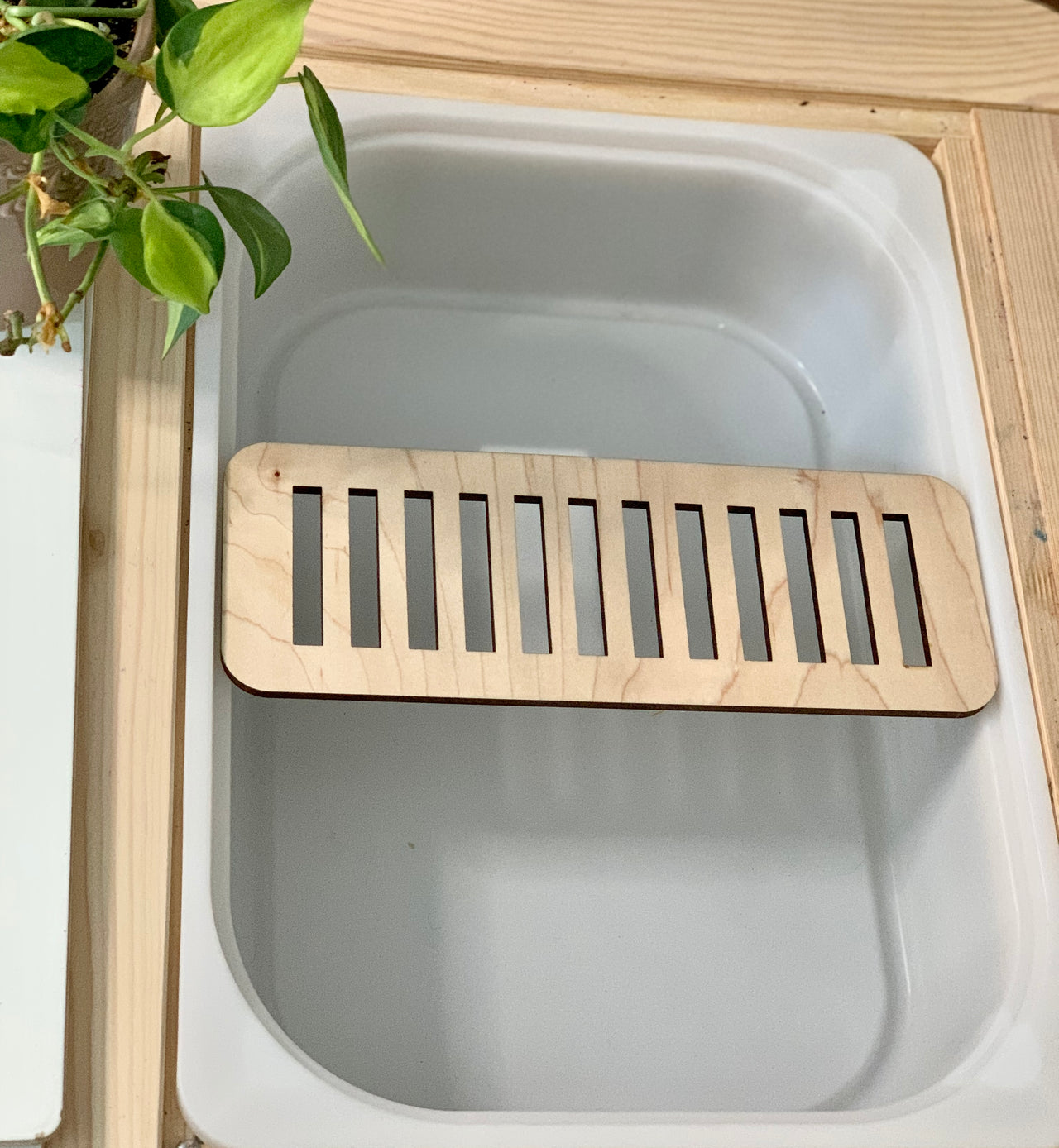 Maple plywood cross piece slot insert fitted inside Trofast Flisat bin with light green plant nearby on wooden surface