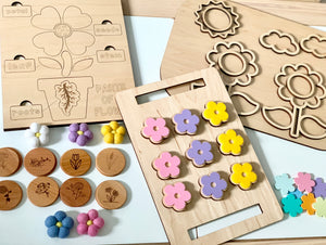 Wooden flower-themed memory game pieces with pastel flower shapes, engraved plant parts, and colorful felt flower tokens on white surface