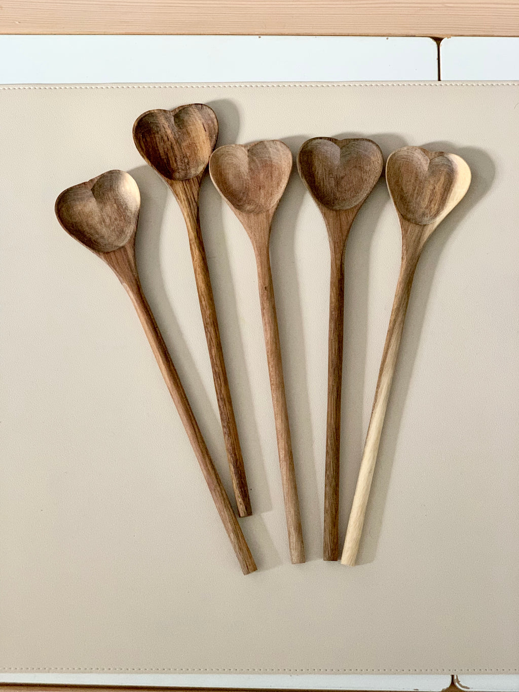 Five natural wooden heart shaped spoons with long handles arranged on beige surface