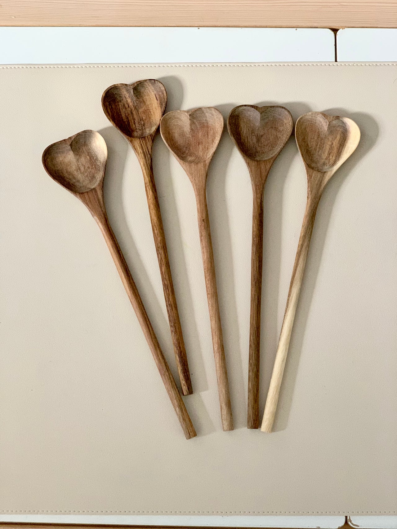 Five natural wooden heart shaped spoons with long handles arranged on beige surface
