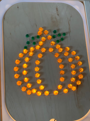 Lighted pumpkin shape made from small orange and green light pegs on light wooden Flisat insert tray